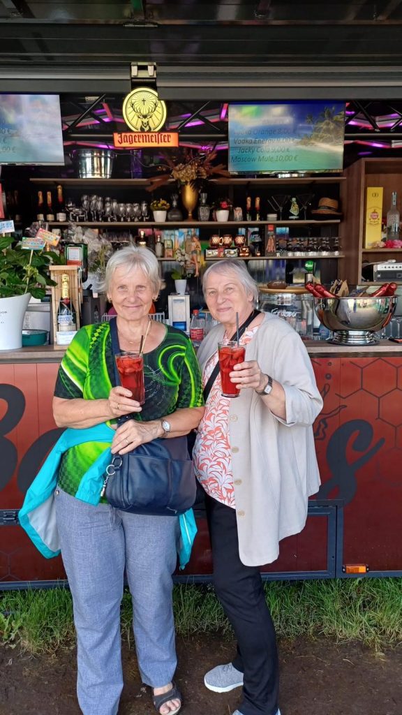 Zwei ältere Damen stehen vor der Bar und trinken Erdbeerbowle.