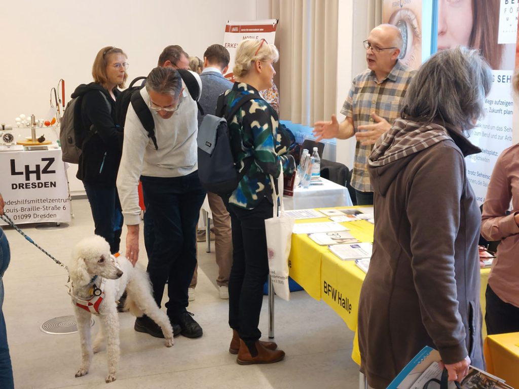 Herr Stemmler vom BFW (Halle) unterhält sich mit einer Besucherin. Ringsherum sind weitere Aussteller und Besucher abgebildet.