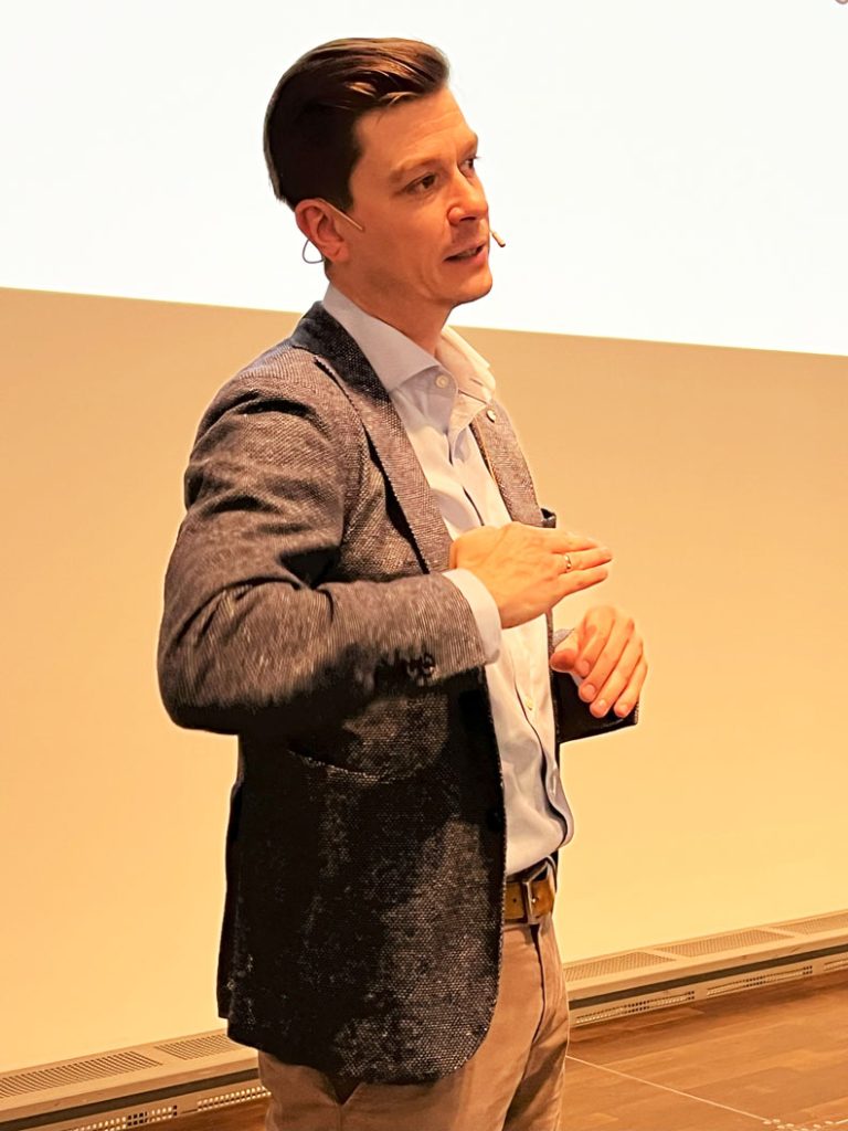 Herr Kolbe, Leiter der Optometrie, REGIOMED Rehaklinik Masserberg gGmbH, stand bei seinem Vortrag „Ophthalmologische Rehabilitation“ auf der Bühne. Er trägt eine beige Hose, ein hellblaues Hemd und einen blau-grau-melierten Sakko.