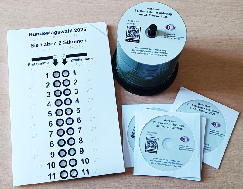 Neben einer Wahlschablone steht ein Stapel fertig gebrannter Info-CDs und drei bereits verpackte Exemplare.